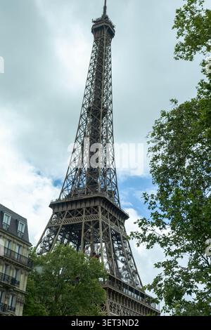 Der Eiffelturm erhebt sich in den Himmel mit Wolken darüber. Bäume sind in der Nähe zu sehen, und Gebäude sind in der Gegend vorhanden. Diese Szene zeigt einen Ruhm Stockfoto