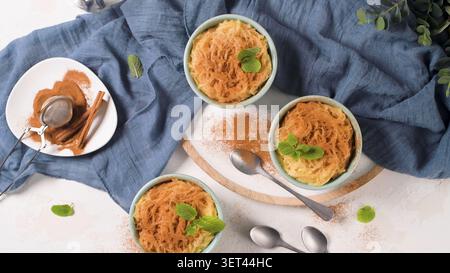 Ein Top-Down-Studio-Shot mit drei Schüsseln süßer Vermicelli-Pasta, gekrönt mit Zimtpulver und frischen Minzblättern, angeordnet auf einer rustikalen weißen Oberfläche Stockfoto