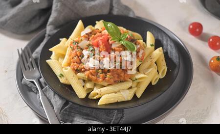 Dieses herzhafte Gericht umfasst perfekt gekochte Penne-Pasta, die mit einer reichhaltigen Tomaten- und Linsensauce überzogen ist. Serviert auf einem dunklen Teller, die lebhaften Farben und frisch Stockfoto