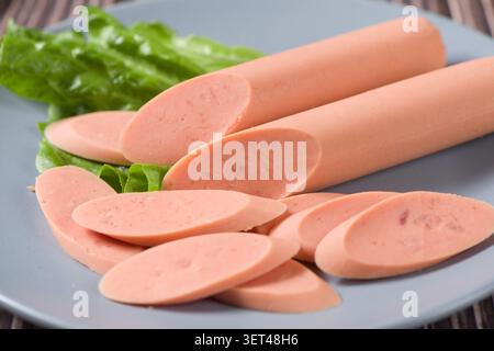 Frankfurter Würstchen in Scheiben geschnitten und auf einem blauen Teller mit frischem Salatblatt serviert Stockfoto