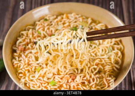 Handhebe Instant Ramen aus einer Schüssel mit Stäbchen auf einem dunklen Holztisch Stockfoto