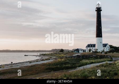 Saaremaa, Estland - 5. Juni 2026: Ruhige Küstenszene mit einem historischen Leuchtturm mit Blick auf eine ruhige Küste und ruhiges Wasser unter weichem Sonnenaufgang Stockfoto