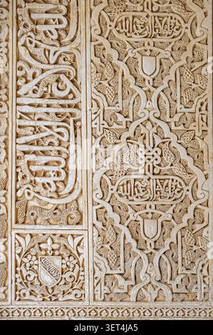 Eine detaillierte Ansicht von geschnitzten arabesken Blumenmustern und arabischer Kalligraphie-Schrift auf einer Gipswand in der Alhambra in Granada, Spanien Stockfoto