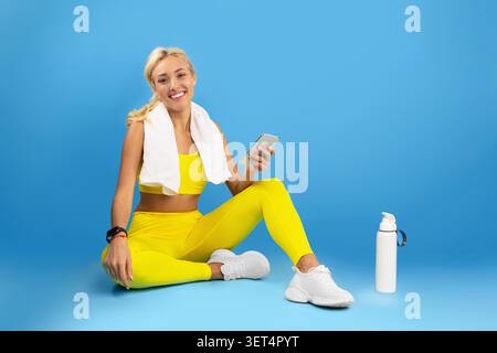 Lächelnde Junge Frau Mit Smartphone Und Wasserflasche Im Fitnessstudio, Fitnesskonzept Stockfoto