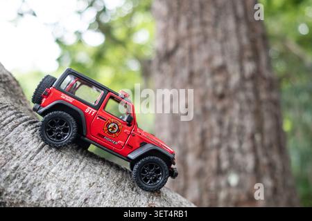 Chiang Mai, Thailand - 19. Juni 2026 : Ein roter Feuerwehrmann Jeep Wrangler Rubicon Druckguss Modellauto klettert einen Baumzweig, Rettungsfahrzeug Spielzeug mit fo Stockfoto