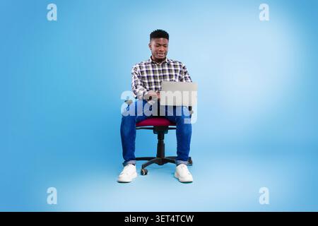 Junger Afroamerikanischer Mann, Der Am Laptop Arbeitet, Während Er Auf Dem Bürostuhl Sitzt, Business Concept Stockfoto