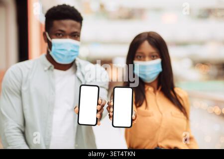 Junger Afroamerikanischer Mann Und Frau, Die Smartphones Mit Leeren Bildschirmen Halten, Inneneinrichtung Stockfoto