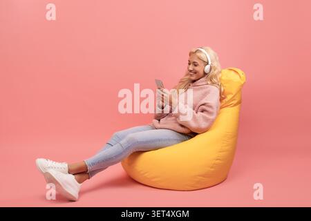 Glückliche Junge Frau, Die Musik Auf Dem Smartphone Genießt, Während Sie Sich Im Sitzsack-Stuhl Entspannt Stockfoto