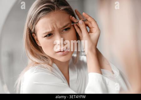 Junge Frau, Die Zu Hause Vor Dem Spiegel Augenbrauen Zupft, Hautpflegekonzept Stockfoto