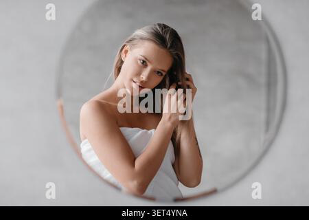 Junge Frau, die zu Hause Haarpflege vor dem Spiegel anwendet, Selbstpflegekonzept Stockfoto