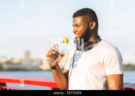 Ein Mann genießt ein erfrischendes Getränk und hört Musik im Freien an einer malerischen Uferpromenade Stockfoto