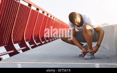 Der Mann passt die Laufschuhe auf der Brücke während des morgendlichen Trainings in urbaner Umgebung an Stockfoto
