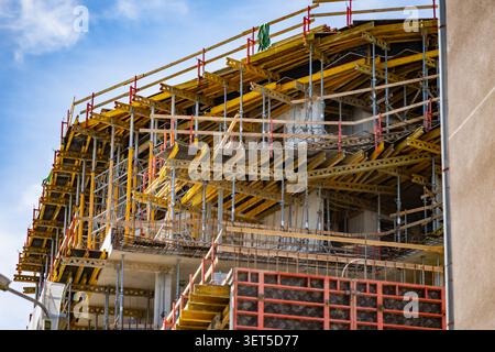 Eine detaillierte Perspektive auf ein mehrstöckiges Appartementgebäude im Bau mit komplexen Gerüstgerüsten und hellgelber Bausubstanz Stockfoto