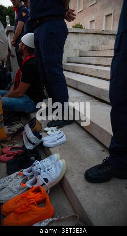 Tirana, Albanien – 20. Juni 2026: Schuhe und persönliche Gegenstände ruhen auf öffentlichen Stufen in der Nähe von Teilnehmern, die an einem überfüllten Protest teilnehmen. Stockfoto