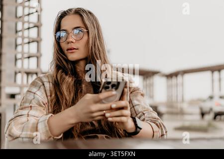 Frau Smartphone draußen junge Frau sitzt auf einer Außenterrasse mit ihrem Handy und blickt nachdenklich weg Stockfoto