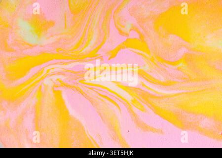 Fließende Acrylmalerei, die einen farbenfrohen abstrakten Hintergrund mit wirbelnden Rosa und Gelb schafft Stockfoto