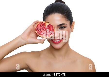 Eine Frau posiert mit einer Granatapfelfrucht in der Hand vor weißem Hintergrund. Das Setting konzentriert sich auf das Thema und die lebendige Frucht. Diese Aufnahme Stockfoto