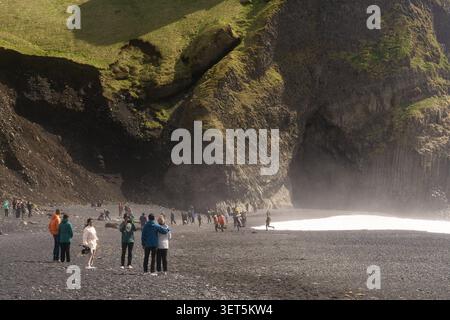 Touristen erkunden den schwarzen Sandstrand und die Basaltklippen an der Reynisfjara bei Vík, Südisland. Stockfoto
