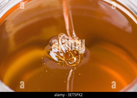 Goldener Honig tropft langsam und bildet eine zähflüssige Textur in einem Glas Stockfoto