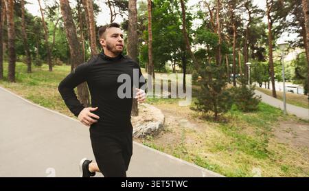 Mann joggt in einem Park, umgeben von Bäumen an einem sonnigen Tag Stockfoto