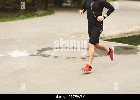 Mann, der tagsüber auf einem Park Path joggt und Sportausrüstung und Kopfhörer trägt Stockfoto