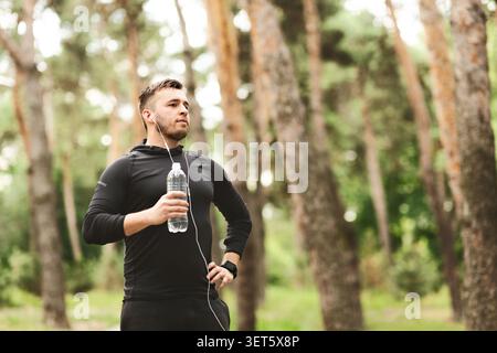 Junger Mann in Fitnesskleidung, der eine Pause macht, während er in einem üppigen grünen Wald läuft Stockfoto