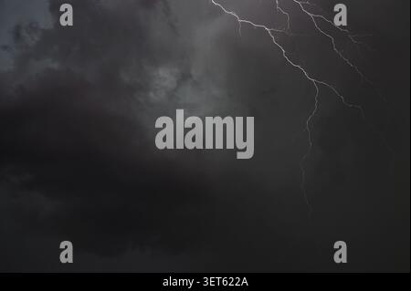 Ein heller weißer Blitz streift über einen dunklen stürmischen Nachthimmel mit unheilvollen Wolken. Stockfoto