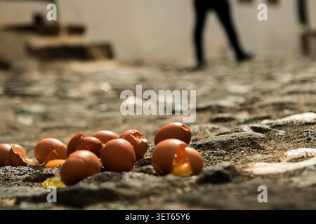 Gebrochene Eierschalen und verschüttetes Eigelb liegen auf einer strukturierten Kopfsteinoberfläche Stockfoto
