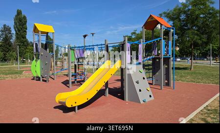Ein modernes öffentliches Spielhaus im Freien verfügt über Doppeltürme mit orangefarbenen und gelben Dächern, eine Seilbrücke und kleine Kletterwände auf einem Schutz Stockfoto