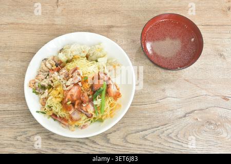 Trockene chinesische Ei gelbe Nudeln mit rotem Barbecue-Schweinefleisch und Knödel mit Krabbenfleisch auf Teller mit klarer Suppentasse Stockfoto