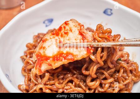 Essstäbchen aus Metall mit rotfermentiertem Kohl über herzhaften Instant-Nudeln aus schwarzen Bohnen, die ein authentisches und beliebtes koreanisches Dining-Menü darstellen Stockfoto