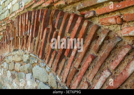 Nahaufnahme diagonal angeordneter Ziegel in einer alten Mauermauer, die historische Bautechniken und verwitterte architektonische Texturen enthüllt. Stockfoto