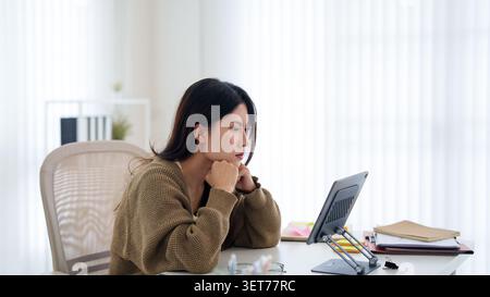 Junge asiatische Frau, die Stress und Frustration erlebt, während sie im Home Office mit natürlichem Licht an einem Tablet arbeitet Stockfoto
