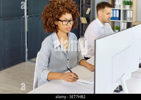 Eine zielgerichtete Geschäftsfrau, die am Computer im Großraumbüro mit einem Kollegen in der Nähe arbeitet Stockfoto