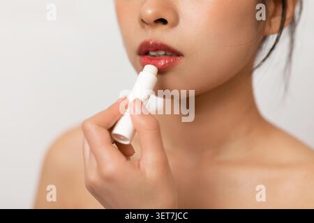 Junge Asiatische Frau, Die Lippenbalsam Aufträgt, Nahaufnahme, Schönheitsroutine Zu Hause Stockfoto
