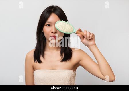 Junge Asiatische Frau, Die Haarbürste Hält Und Hockt, Hautpflege-Routine Zu Hause Stockfoto