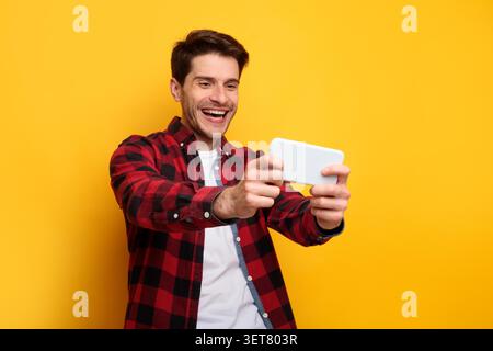 Glücklicher Junger Mann, Der Mobiles Spiel Mit Smartphone Spielt, Lächelnd, Gelber Hintergrund Stockfoto