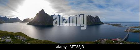 Atemberaubender Panoramablick auf die Lofoten-Inseln mit dramatischen zerklüfteten Gipfeln, unberührtem Wasser und einem kleinen Küstendorf auf dem Stockfoto