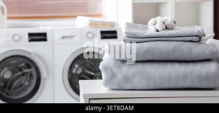Frisch gewaschene Baumwollbettwäsche und Handtücher mit Baumwollballen in einem hellen Waschraum, Baumwollballen liegen auf der sauberen Bettwäsche, was die betont Stockfoto