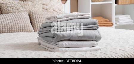 Frisch gewaschene weiße und graue Bettwäsche auf einem gemütlichen Bett mit Kissen. Das Bett verfügt über weiche Kissen und eine strukturierte Decke Stockfoto