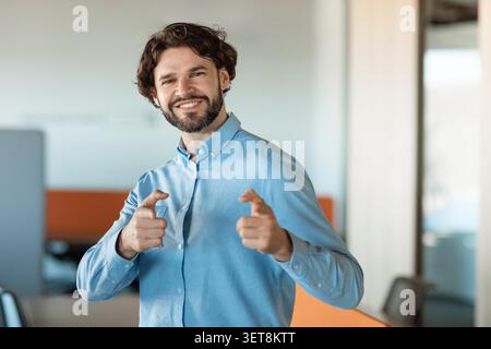 Glücklicher Junger Mann, Der Lächelt Und Zeigt In Büro, Geschäftskonzept Stockfoto