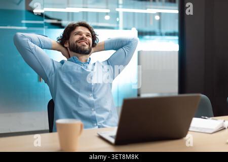 Glücklicher Mann, Der Sich Im Büro Mit Laptop Und Business-Konzept Entspannt Stockfoto