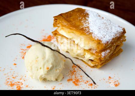 Ein Mille-Feuille-Dessert steht auf einem Teller neben einer Schaufel Vanilleeis. Die Blätterteigschichten sind mit Creme gefüllt. Stockfoto