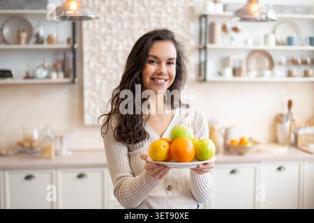 Lächelnde Junge Frau, Die Platte Mit Frischen Früchten In Der Modernen Küche Hält, Gesundes Lifestyle-Konzept Stockfoto