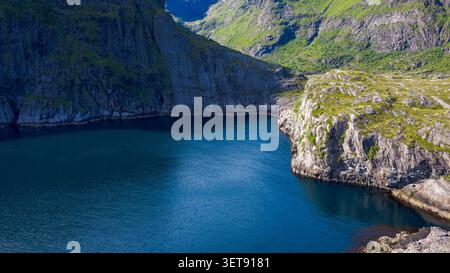 Atemberaubender Panoramablick auf einen tiefblauen Bergsee, umgeben von hohen felsigen Klippen und üppigen grünen Berghängen auf den Lofoten Inseln Stockfoto