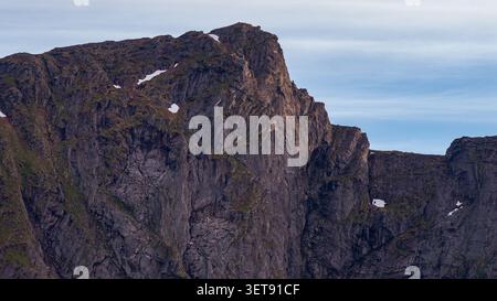 Ein beeindruckender Panoramablick auf die charakteristischen Säulen-Basaltgipfel der Lofoten mit Schnee, moosbedeckten Hängen und zerklüfteten Felsen Stockfoto