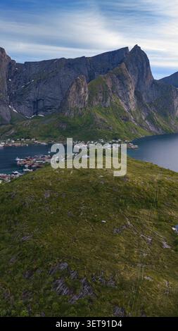 Atemberaubendes Panorama der Lofoten Islands mit dramatischen zerklüfteten Gipfeln, grünen Hügeln und malerischem Küstendorf, das sich unterhalb der Höhe erhebt Stockfoto