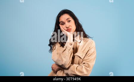 Gelangweilte Hispanische Frau Ruht Kopf Auf Der Hand, Studio Mit Blauem Hintergrund Stockfoto