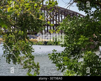 Pittsburgh Pennsylvania USA – 21. Juni 2026: Brücke aus Industriestahl, die sich über das Flusswasser erstreckt und durch saftig grüne Sommerblätter gesehen wird Stockfoto