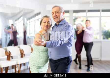 Paare reifer Amateurtänzerinnen führen enthusiastisch romantischen Tangotanz im Tanzsalon auf Stockfoto